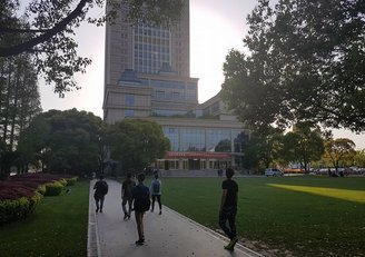 Campus der Fudan Universität in Shanghai: großes Gebäude und eine weitläufige Parkanlage mit Studenten.