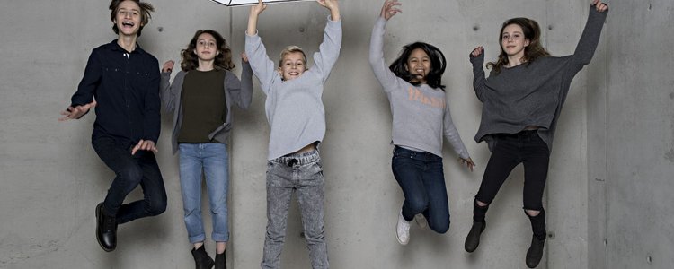 Fünf Kinder springen in die Höhe, einer hält einen großen Bleistift aus Karton in den Händen.