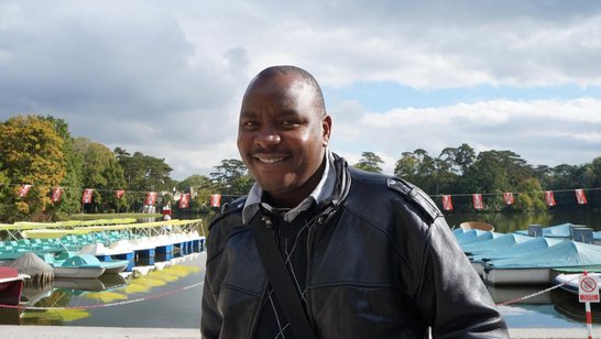 A man is standing in front of a lake and smiling into the camera.