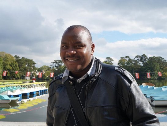 A man is standing in front of a lake and smiling into the camera.