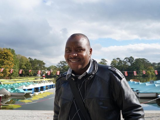 A man is standing in front of a lake and smiling into the camera.