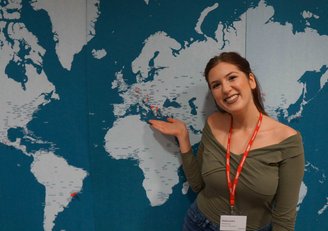 Eine Stipendiatin des OeAD zeigt mit ihrer Hand auf eine Weltkarte, die hinter ihr an der Wand hängt.