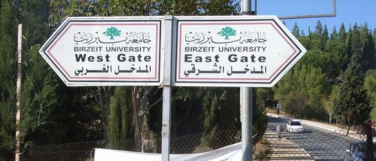 Two signs standing on the roadside in front of a fence