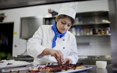 Junge Frau in Kochuniform garniert Essen in Küche