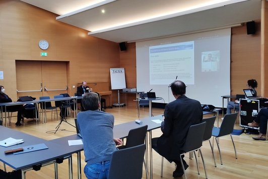 Mehrere Personen sitzen im Rahmen der Breakout-Session an einem Tisch in U-Form und schauen konzentriert eine Präsentation an. 