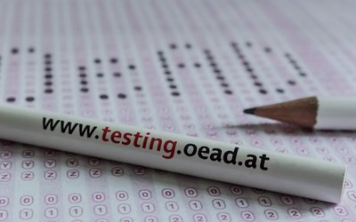 Bleistift mit Aufschrift "OeAD International Testing Services" liegt auf einem Blatt Papier.