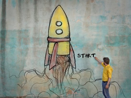 Mann zeichnet das Wort "Start" auf eine Wand, auf der eine Rakete aufgezeichnet ist.