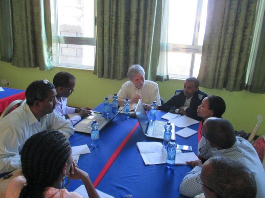 Group of people sitting around a table looking to one talking man