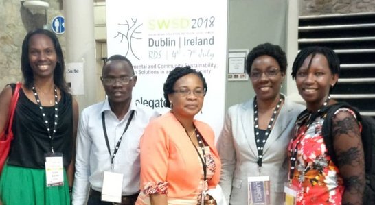 Five people posing for a group photo in front of a big conference poster