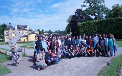 Die Stipendiaten bei einem Gruppenfoto vor einem Schloss mit Park und Einhornstatuen in Salzburg.