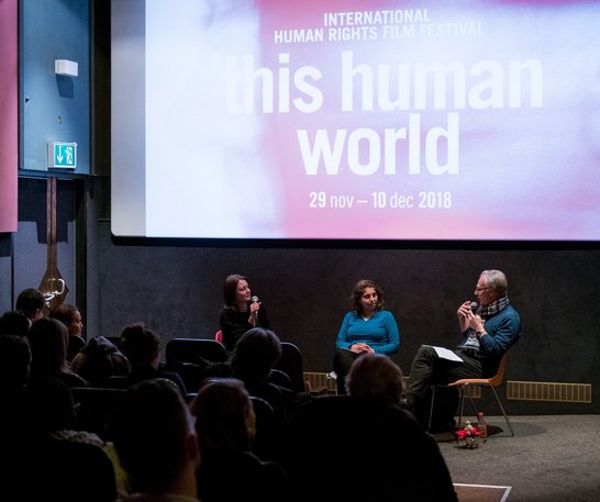 picture shows people in the cinema sitting, listening and watching the two panellists who are sitting in the front of the room