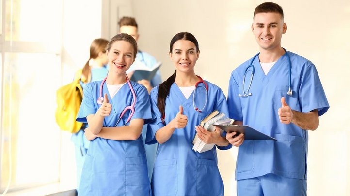 Eine Gruppe von Medizinstudieren zeigt das Daumen-Hoch-Symbol im Eingangsbereich einer Klinik