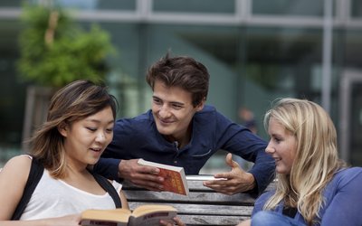 Drei Studierende beim Diskutieren im Freien auf einer Bank