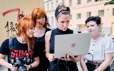 Vier junge Frauen mit einem Laptop und einer Kamera stehen auf der Straße