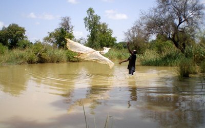 Ein Fischer steht in einem Fluß und wirft ein Fischernetz aus. 