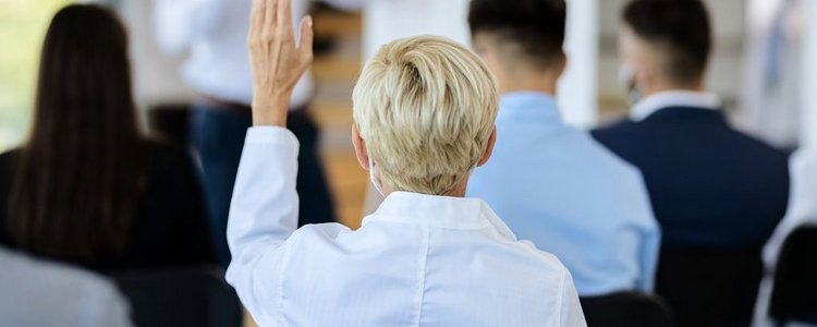 back view of businesswoman attending a seminar and raising her arm to ask a question.