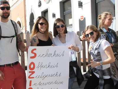 Group of people with sunglasses holding up a poster with a slogan on it