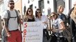 Group of people with sunglasses holding up a poster with a slogan on it