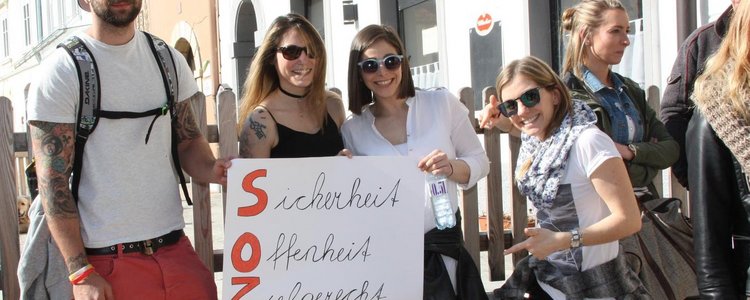 Group of people with sunglasses holding up a poster with a slogan on it