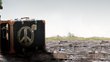 An old suitcase with a peace symbol painted on it. The suitcase is on the ground outside.