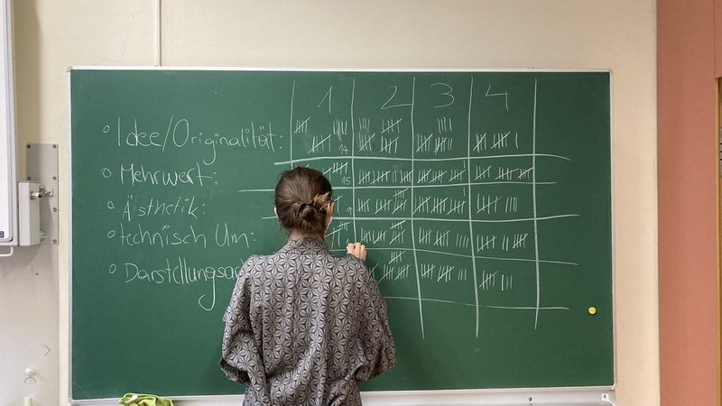 Eine Junge Dame die auf einer Tafel Punkte von unterschiedlichen Teams bei unterschiedlichen Disziplinen mitschreibt.