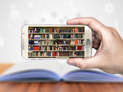 Hand mit Smartphone auf dem ein Foto eines Bücherregals zu sehen ist