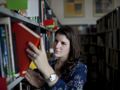 Frau nimmt ein Buch aus einem Bücherregal