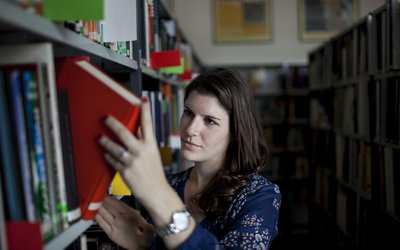 Frau nimmt ein Buch aus einem Bücherregal