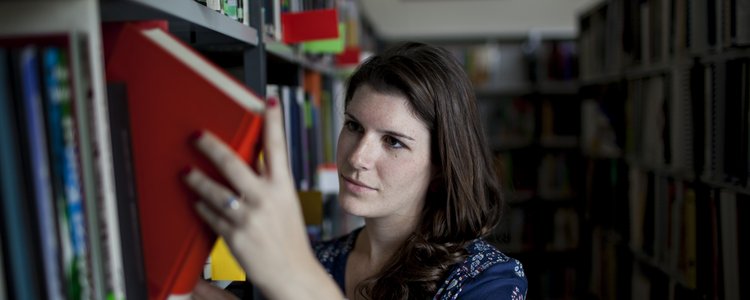 Frau nimmt ein Buch aus einem Bücherregal