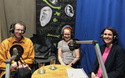 Drei Personen sitzen im Radiostudio vor dem Mikrofon