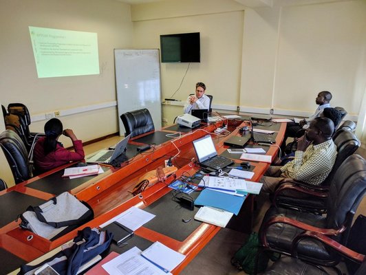 five people sitting around a big table and looking at the presentation 
