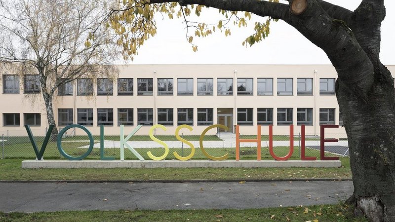 Die Volkschule Wolkersdorf. Vor der Schule steht das Wort Volkschule in einem Farbverlauf geschrieben.