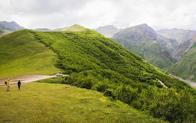 Landschaft im Kaukasus-Gebirge mit grünen Wiesen und Bergen sowie zwei Menschen.