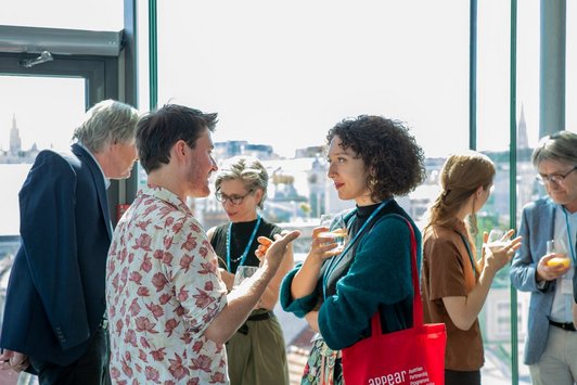 Networking in der Pausenzeit: mehrere Personen unterhalten sich gemütlich vor einer Glaswand mit Ausblick auf Wien