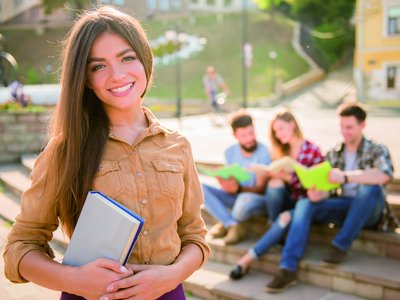 Mädchen hält ein Buch in der Hand, im Hintergrund sind drei Studierende