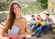 Mädchen hält ein Buch in der Hand, im Hintergrund sind drei Studierende