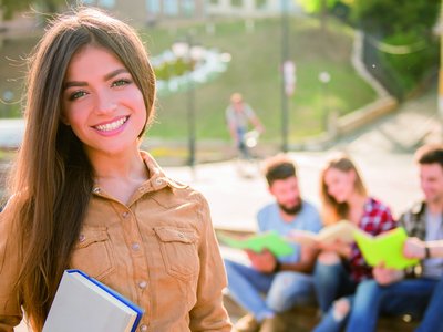 Mädchen hält ein Buch in der Hand, im Hintergrund sind drei Studierende