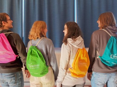 Vier Schülerinnen und Schüler stehen mit dem Rücken zur Kamera und tragen Erasmus+ Turnsäcke