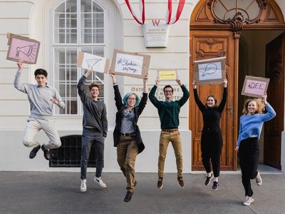 Junge Studierende hüpfen in die Luft und halten Schilder in der Hand