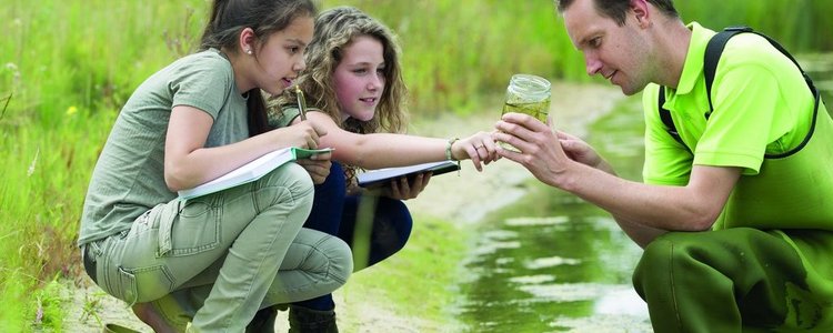 Zwei Schülerinnen und ein Forscher entnehmen eine Wasserprobe