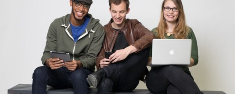 Drei Studierende, zwei Männer, eine Frau, die einen Laptop in der Hand hält.