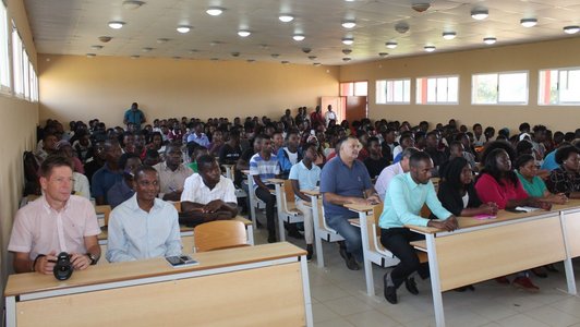 A hall full of people sitting arranged in rows and watching something in the front