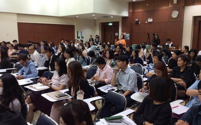 Großer Saal mit vielen Tischen, die in Reihen stehen und vielen thailändischen Studenten.