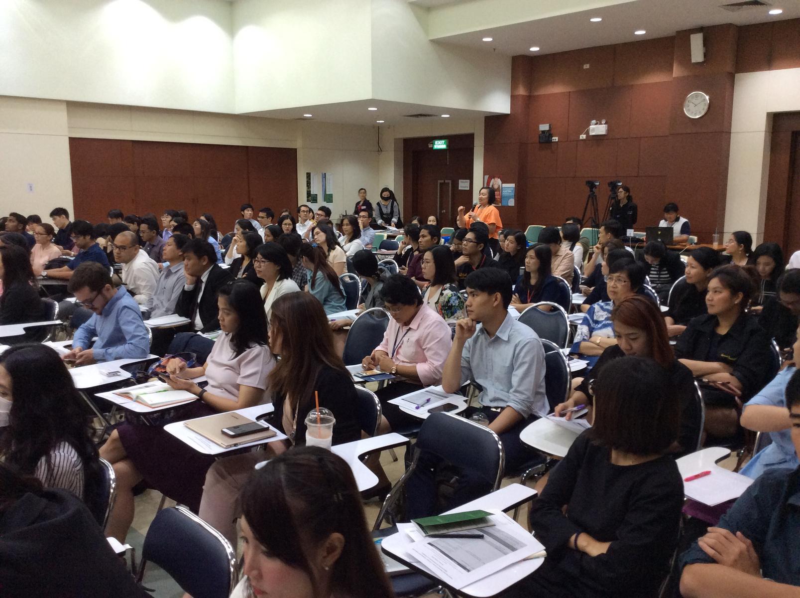 Large hall with many tables arranged in rows and many Thai students.