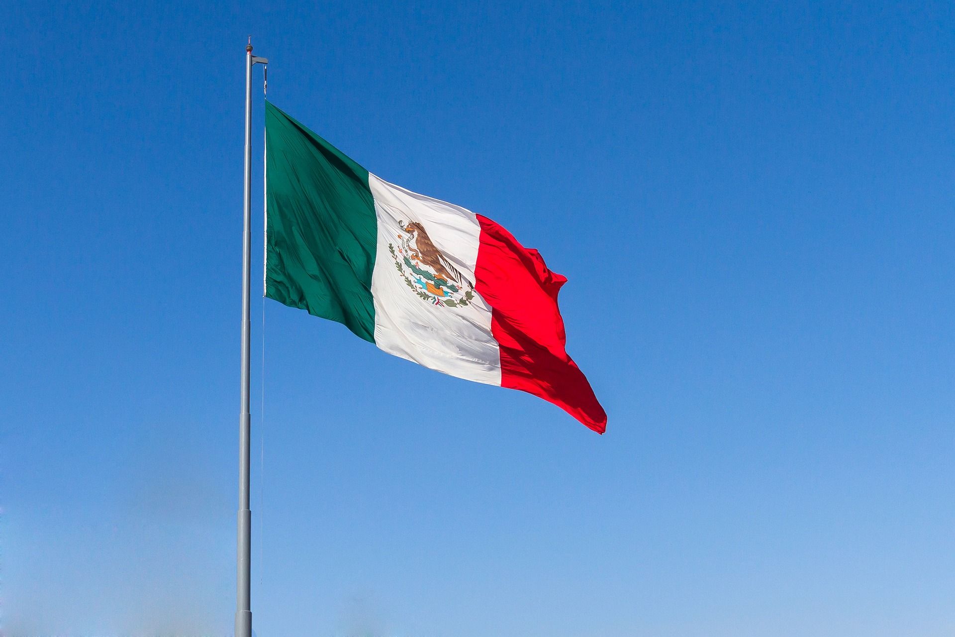 A Mexican flag blows in the wind in the background of the clear blue sky.