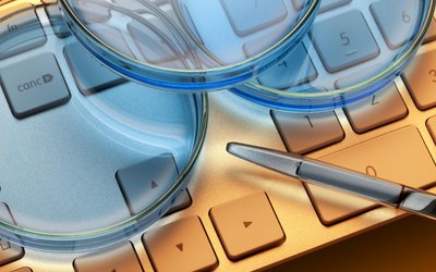 Ausschnitt einer Computertastatur mit drei daraufliegenden flachen hellblauen runden Glasobjekten und eine Pipette