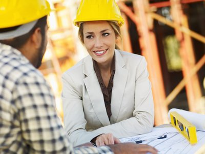 Frau und Mann mit Bauhelmen auf einer Baustelle