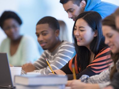 Studierende unterschiedlicher Ethnien mit Büchern und Laptop bei einer Gruppenarbeit