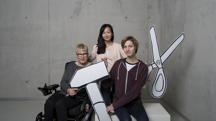 Drei Personen, davon eine im Rollstuhl, mit Hammer und Schere